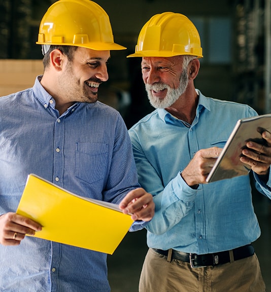 two business guys wearing yellow hats and going over information on ipad