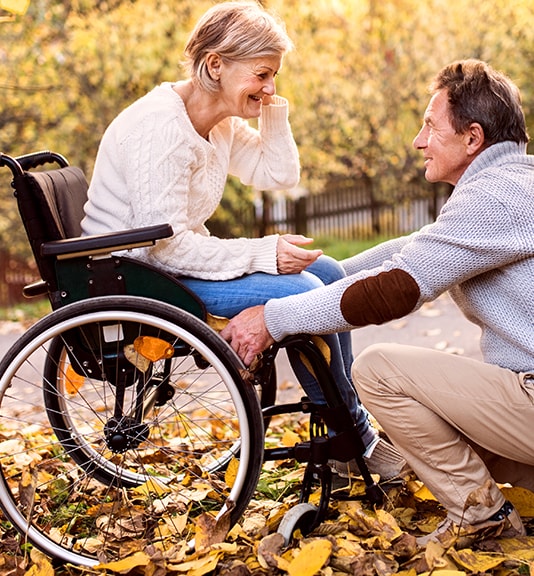 elderly man kneeling and talking to his wife in wheelchair