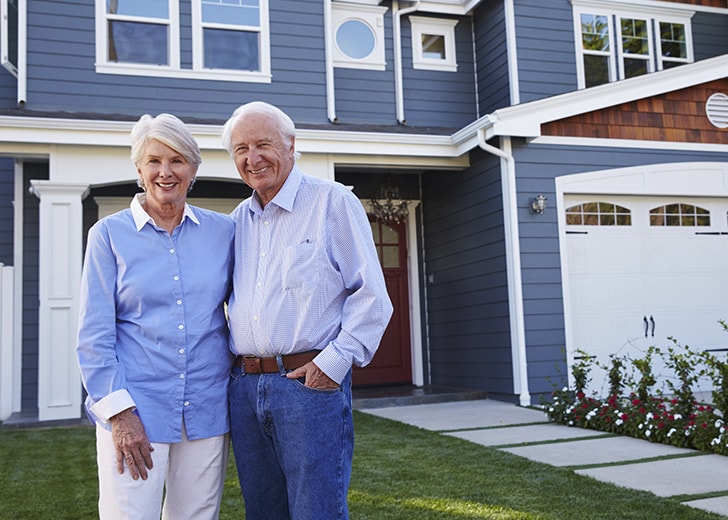 senior couple standing in front of home