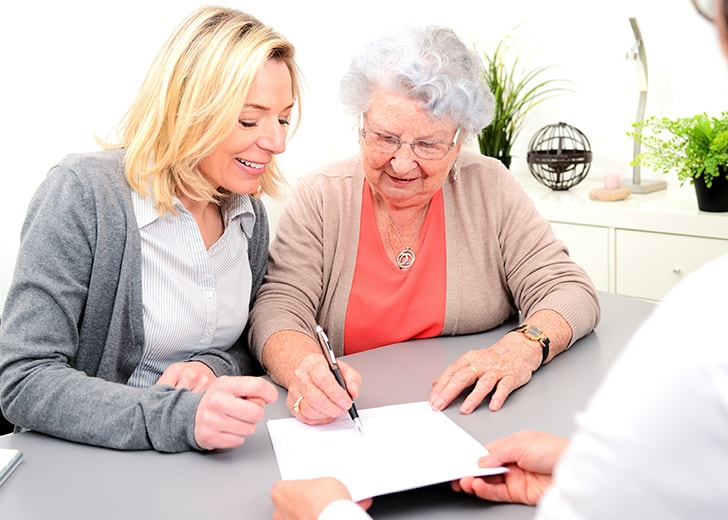 elderly woman sitting next to woman writing out her living will