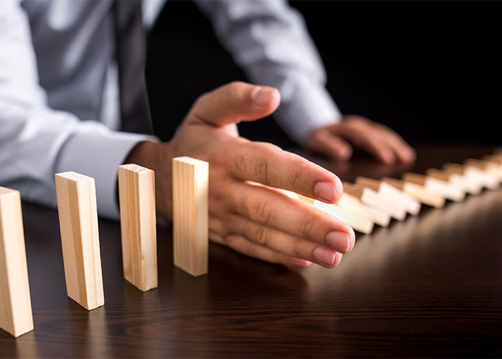 man holds out hand to stop blocks from falling, concept of asset protection