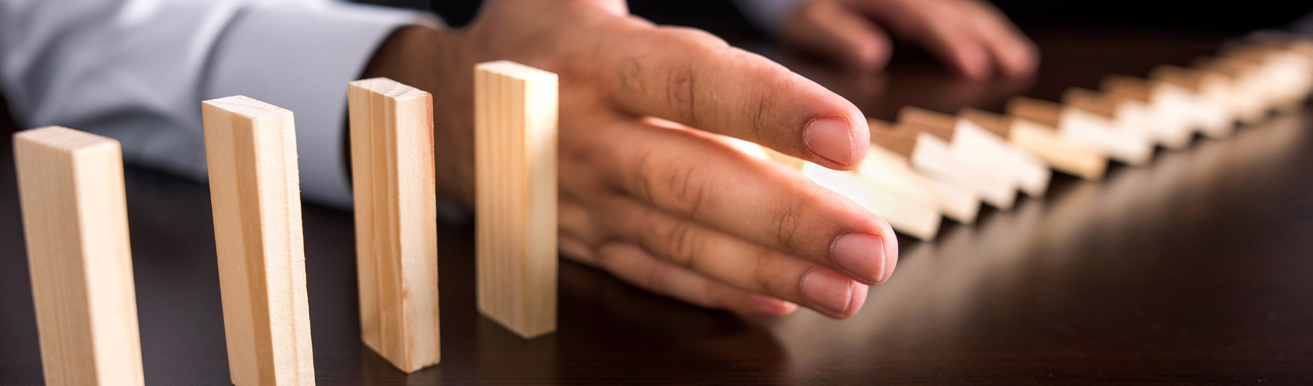 man holds out hand to stop blocks from falling, concept of asset protection